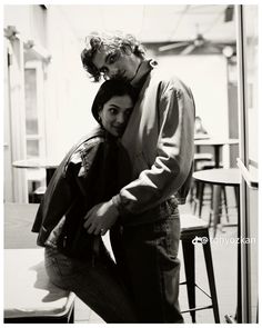 black and white photograph of a man hugging a woman in front of a table with chairs