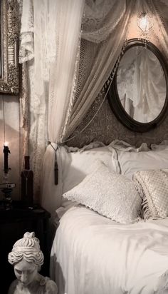 a white bed topped with lots of pillows next to a round mirror and table lamp