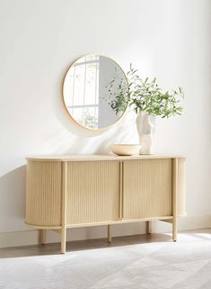 a white room with a round mirror on the wall and a plant in a vase