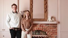 a man and woman standing next to each other in front of a brick fire place