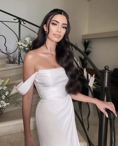 a woman in a white dress posing for a photo on the stairs with flowers behind her