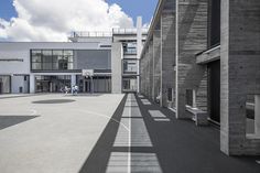 an empty basketball court surrounded by buildings and people on the other side with clouds in the sky