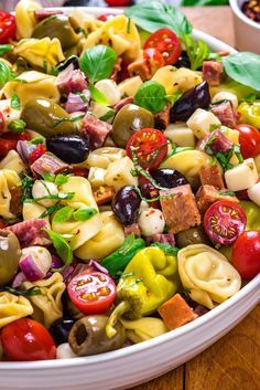 pasta salad with tomatoes, olives, and other vegetables in a white bowl on a wooden table