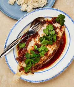 a white plate topped with fish covered in sauce and cilantro next to rice