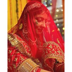 a woman in red and gold is looking at her cell phone while wearing a veil