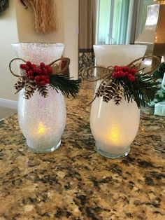 two glass vases with pine cones and red berries are sitting on a granite countertop