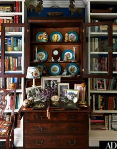 a bookcase filled with lots of books next to a wooden dresser topped with plates