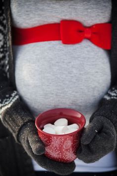 a person holding a cup with marshmallows in it's hands and wearing a red bow tie