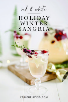 two glasses filled with white wine sitting on top of a wooden cutting board next to christmas decorations