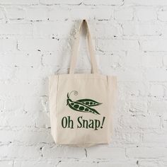 a tote bag hanging up against a white brick wall with the words oh snap on it