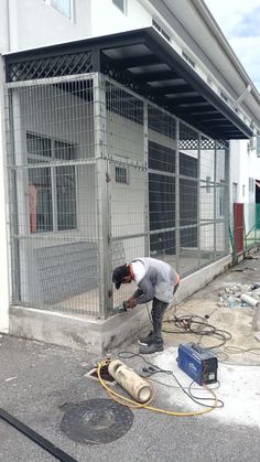 a man is working on the side of a building in front of a large cage