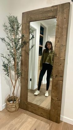 a woman standing in front of a mirror with her reflection on the floor next to a potted plant