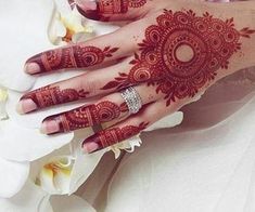 a woman's hand with henna tattoos on it and flowers in the background