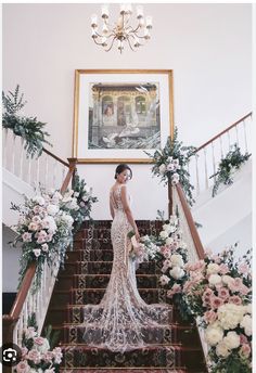 a woman in a wedding dress standing at the top of stairs with flowers and greenery