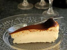 a piece of cheesecake on a glass plate with wine glasses in the back ground