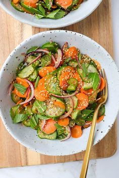 two white bowls filled with salad on top of a wooden cutting board next to a gold fork