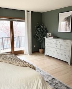 a bedroom with green walls, white furniture and a large sliding glass door that leads to a balcony