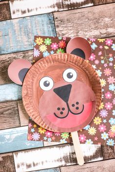 a paper plate shaped like a bear with flowers on it and a wooden stick sticking out of its mouth