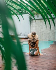 a woman sitting on the ground in front of a pool wearing a sunhat and hat