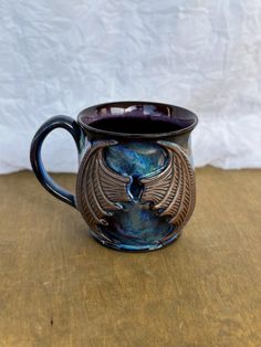 a coffee mug with a dragon design on it sitting on a wooden table next to a white wall