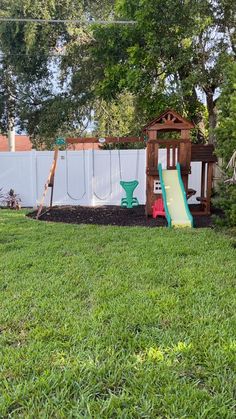 a backyard with a play set and slide in the grass next to a white fence