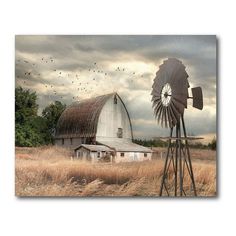 an old barn with a windmill in the foreground and birds flying over it on a cloudy day