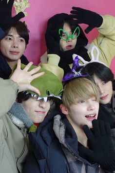 group of young men posing in front of a pink wall with their hands up to the camera