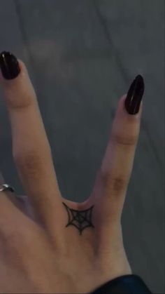 a woman's hand with a black spider tattoo on her left thumb and finger