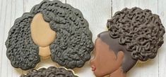 three cookies decorated to look like women's hair are on a white wooden surface