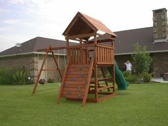 a wooden swing set with a slide and climbing frame in front of a brick house