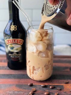 a person pouring coffee into a glass filled with ice cream and nuts next to a bottle of bailey's