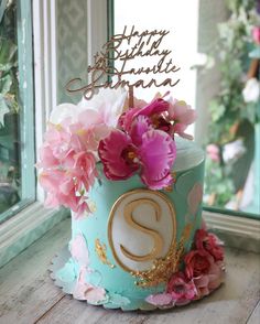 a birthday cake decorated with flowers and the letter s on top is sitting in front of a window