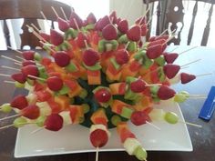 a bunch of skewered fruit sitting on top of a white plate next to a wooden table