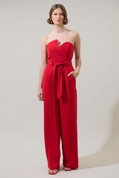 We don't know about you, but we're totally love this one! This trendy jumpsuit has an asymmetrical swoosh neckline in the front. Fitted waist tops wide legs that have front pockets and a belt. Wear this jumpsuit with heels for a fancy look. - Belted- Strapless- Pockets- Zipper- Comes in 2 colorsSize + Fit - Model is 5'8" and wearing size XS- Measurements taken from size S - Chest: 15 3/4"- Inseam: 33 3/4" Fabric Self: 100% Polyester Style Number P2970 Jumpsuit With Heels, Denim Tube Top, Trendy Jumpsuit, Ruffle Jumpsuit, Strapless Jumpsuit, Red Jumpsuit, Body Dress, Wide Legs, Black White Red