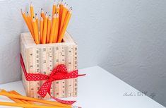 several pencils in a wooden box with a red bow on the top and two orange ones next to them