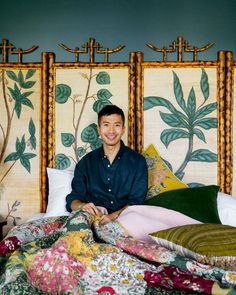 a man sitting on top of a bed in front of two wall hangings with plants