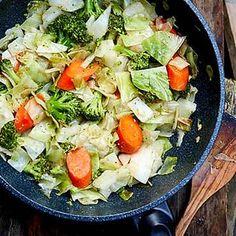 a skillet filled with vegetables on top of a wooden table next to utensils