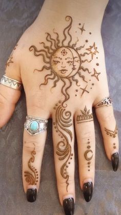 a woman's hand with henna tattoos and rings on her fingers, showing the sun