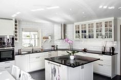 a kitchen with white cabinets and black counter tops is pictured in this image, there are chairs around the island