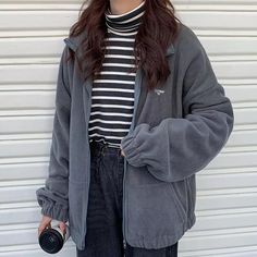 a woman standing in front of a garage door wearing a gray jacket and black pants