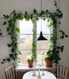 some plants are growing on the window sill in front of a white table and chairs