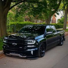 the black truck is parked on the side of the road in front of some trees