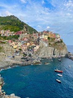 boats are floating in the water near a small village on top of a cliff overlooking the ocean