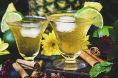 two glasses filled with liquid next to cinnamons and flowers