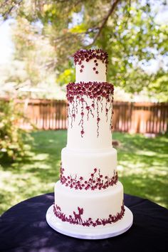 a three tiered white cake with red flowers on it sitting on a black table