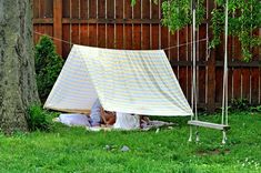 a white tarp is set up in the yard next to a tree and swing