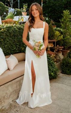 a woman in a white dress standing next to a couch with flowers and greenery