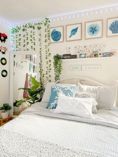 a white bed topped with lots of pillows next to a wall covered in green plants