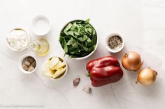 an assortment of vegetables and spices on a white counter top, including tomatoes, onions, spinach