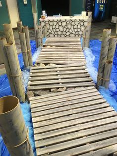 a wooden walkway made out of wood sticks and blue tarp in an indoor area